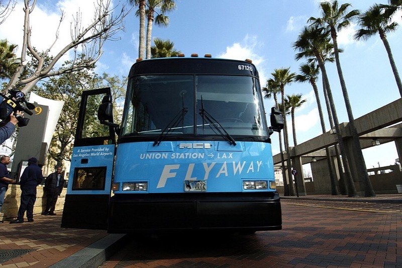 A blue LAX FlyAway coach parked at palm-lined Union Station